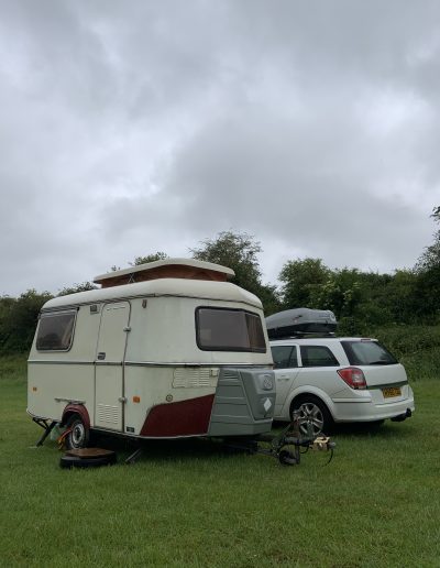 a small caravan and white car in a field