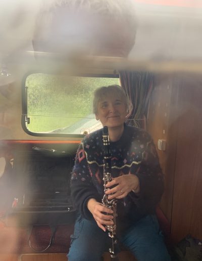 a woman sits in a caravan holding a clarinet looking out of a rain splattered window
